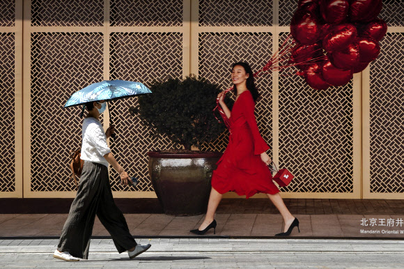 지난 25일 중국 베이징에서 한 여성이 양산을 쓰고 왕푸징 지역의 호텔을 지나가고 있다. 베이징 AP 연합뉴스