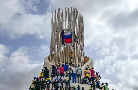 니제르의 쿠데타를 지지하는 이들이 독립기념일인 3일(현지시간) 수도 니아메의 독립 기념탑에 올라가 러시아 국기를 내걸고 있다. 니아메 AP 연합뉴스