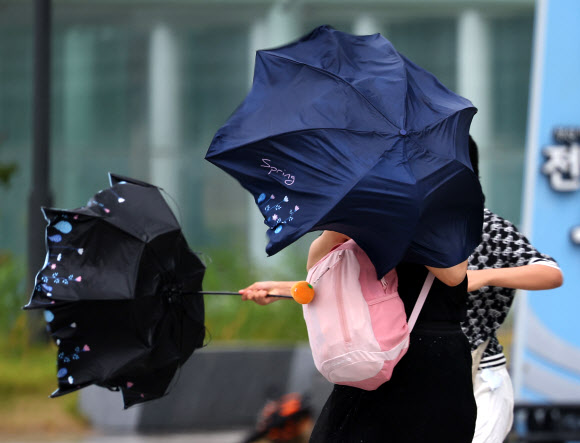 제6호 태풍 ‘카눈’이 북상하고 있는 9일 부산 해운대구 엘시티 인근에 태풍이 몰고온 강한 바람에 빌딩풍이 더해져 우산을 쓴 관광객이 힘겹게 걸어가고 있다. 2023.8.9 연합뉴스