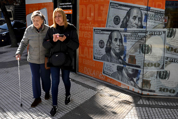 아르헨티나의 두 여성이 대통령 선거 예비선거 다음날인 14일(현지시간) 수도 부에노스아이레스의 100달러 지폐들 이미지 앞을 지나가고 있다. 이날 금융당국은 중앙은행 기준금리를 무려 21%나 올려 세 자릿수를 만드는 초강수를 뒀다. 부에노스아이레스 AFP 연합뉴스