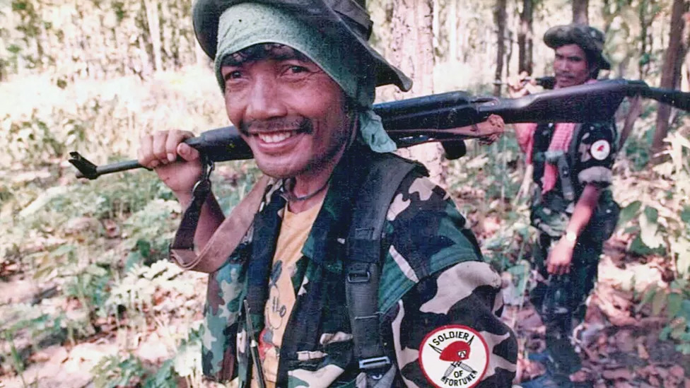 1990년대 캄보디아 정글에서 AK47 소총을 늘 지니고 다니던 힌 니에. 티셔츠에 미키마우스가 눈에 들어오고, 군복 견장에 영어로 ‘운 좋은 병사’가 새겨진 것도 흥미롭다. 마이클 헤이예스 제공 영국 BBC 홈페이지 캡처