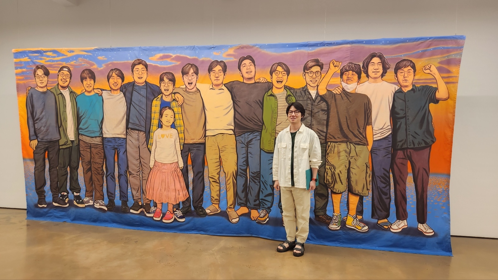 이우성 작가가 자신의 대형 걸개 그림 ‘해질녘 노을빛 친구들’ 앞에서 포즈를 취하고 있다. 정서린 기자