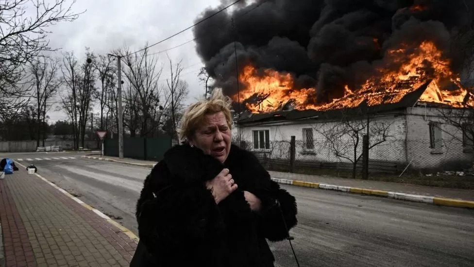 지난해 3월  우크라이나 수도 키이우 근처 이르핀에서 화염에 휩싸인 주택 근처를 지나며 어쩔 줄 몰라하는 여성. AFP 자료사진