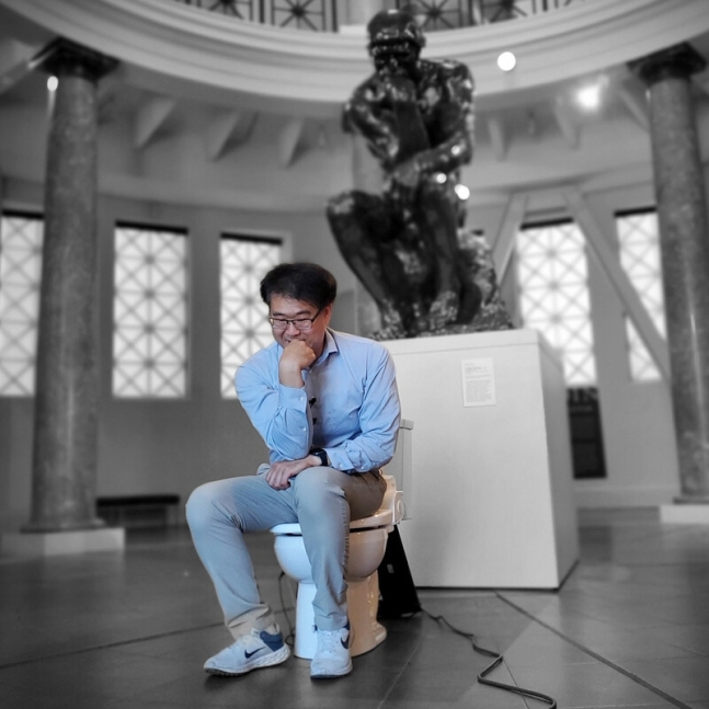 올해 이그노벨상을 수상한 박승민 박사가 스탠퍼드대에 있는 ‘생각하는 사람’ 조각상 앞에서 자신이 개발한 스마트 변기에 앉아 있다. 박 박사 트위터 캡처