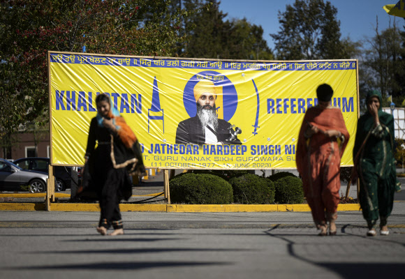 캐나다 브리티시컬럼비아주 서리에 사는 시크교도 여성들이 18일(현지시간) 분리주의 운동 지도자로 지난 6월 총격을 받고 세상을 떠난 하르딥 싱 니자르의 사진이 들어간 칼리스탄 건국 플래카드 앞을 걸어가고 있다. 더 캐너디언 프레스 AP 연합뉴스