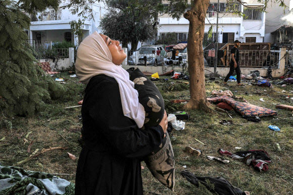 베개를 든 여인이 전날 폭발로 많은 인명이 희생된 가자시티의 알아흘리 아랍병원 마당에 18일(현지시간) 황망한 얼굴로 하늘을 올려다 보고 있다. 가자시티 AFP 연합뉴스