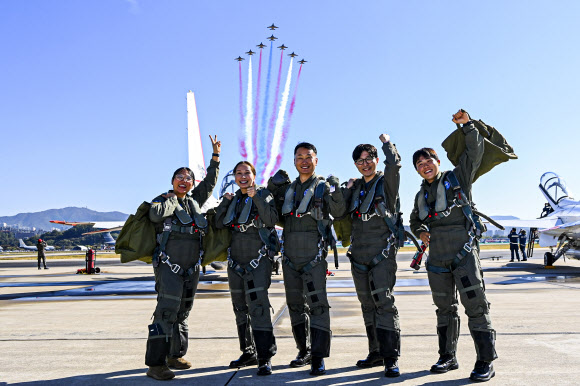 21일 공군 서울공항에서 국민조종사와 명예조종사들이 국산 초음속 고등훈련기 T-50 체험비행에 앞서 비행하는 블랙이글스를 배경으로 기념촬영하고 있다. 왼쪽부터 미셸 장·이호정·김종섭·김의현·유동현 씨. 2023.10.21. 공군 제공