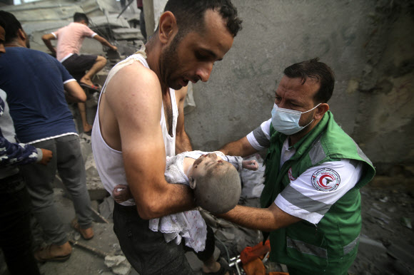 팔레스타인 응급의가 22일(현지시간) 가자지구 남쪽 끝 라파에서 이스라엘군의 공습에 무너진 건물 잔해 더미에서 한 아기를 끄집어내고 있다. 라파 AP 연합뉴스