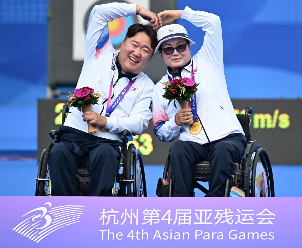한국 양궁 국가대표 김옥금(오른쪽)-박홍조가 26일 중국 항저우 푸인인후 스포츠센터에서 열린 아시안패러게임 혼성 W1 복식 시상식에서 금메달을 목에 걸고 하트를 그리며 기뻐하고 있다. 대한장애인체육회 제공