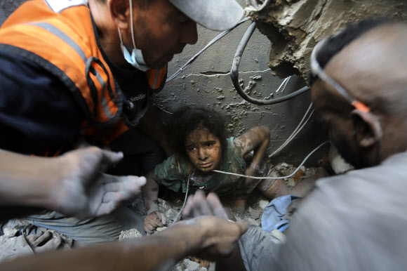 팔레스타인 사람들이 1일(현지시간) 이스라엘군의 공습으로 가자지구 자발리아 난민촌의 무너진 건물 잔해에서 한 소녀를 끄집어내고 있다. 하마스와 이스라엘의 무력충돌 25일 만에 3600명의 어린이가 목숨을 잃었다. 자발리야 AP 연합뉴스