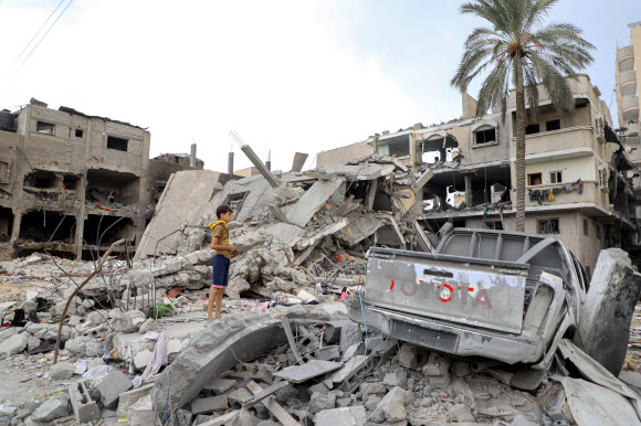 12일(현지시간) 오전  팔레스타인 가자지구 남부 칸유니스의 소년이 두 손으로 무언가를 받쳐든 채 전날 밤 이스라엘군의 공습으로 완전히 부서진 건물 잔해더미를 바라보고 있다. 가자지구에 대한 이스라엘의 보복 공격으로 지금까지 약 1만 1천180명이 숨지고 약 2만8천 명이 다친 것으로 집계됐다. 2023.11.13. 신화 연합뉴스