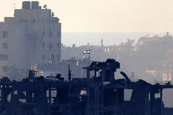 이스라엘 국기가 18일(현지시간) 가자지구의 파괴된 건물 지붕 위에서 펄럭이는 장면이 멀리 이스라엘 남부에서 포착됐다. 로이터 연합뉴스