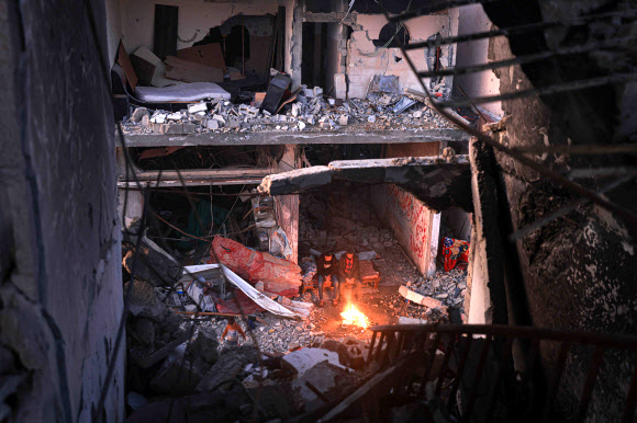 팔레스타인 사람들이 일시 휴전 이레째인 지난달 30일(현지시간) 가자지구 남부 칸 유니스의 외곽 키자 지구 파괴된 건물에서 밤을 지새며 모닥불을 쬐고 있다. 칸 유니스 AFP 연합뉴스