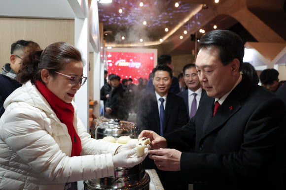 윤석열 대통령이 7일 오후 서울 중구 동대문디자인플라자(DDP)에서 열린 2023년 눈꽃 동행축제 개막행사를 마친 뒤 안흥찐빵 부스를 찾아 찐빵을 건네받고 있다. 2023.12.7  대통령실 제공