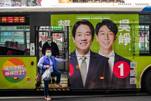 한 대만 시민이 27일 대만 집권여당인 민진당 라이칭더(가운데) 대선후보의 얼굴이 실린 광고로 도배된 버스에서 내리고 있다. 타이베이  AFP 연합뉴스