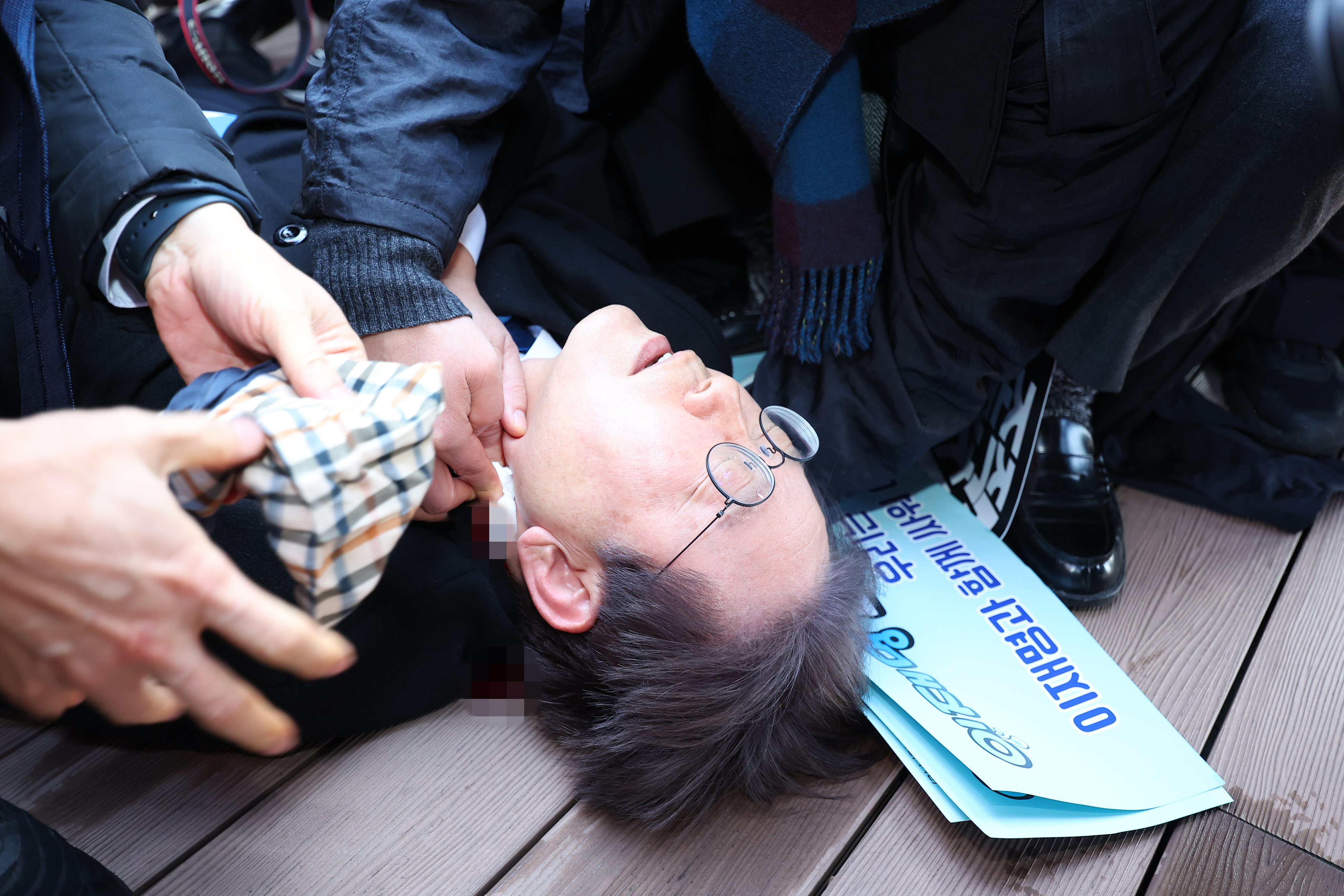 이재명 더불어민주당 대표가 2일 부산 가덕도 신공항 부지를 둘러본 후 기자들과 문답을 진행하던 중 왼쪽 목 부위에 습격을 당해 피를 흘린 채 쓰러져 있다. 2024.1.2 부산 연합뉴스