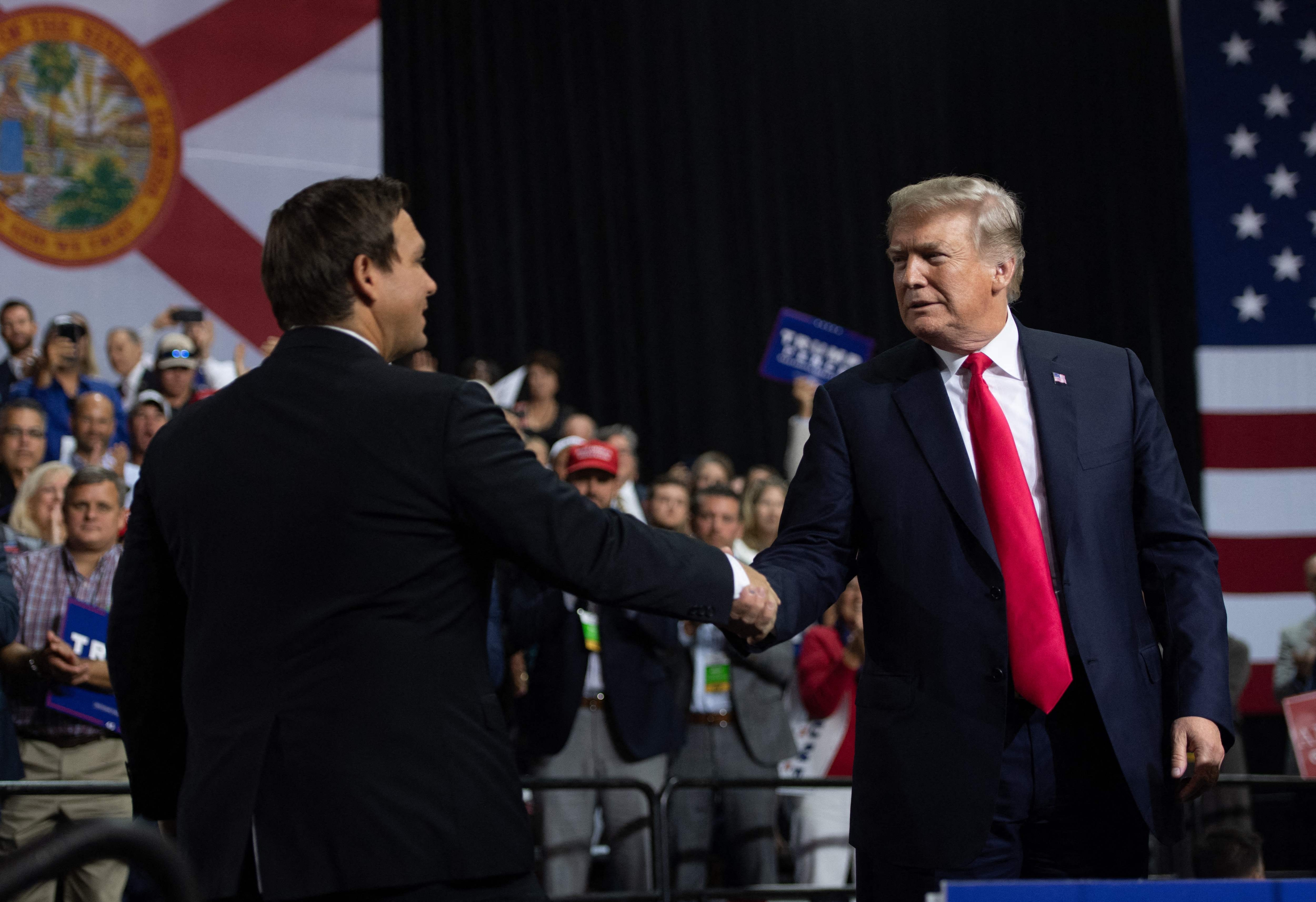 21일(현지시간) 론 디샌티스(왼쪽) 플로리다 주지사가 도널드 트럼프 전 대통령과 플로리다 유세 도중 악수를 나누고 있다. AFP 연합뉴스