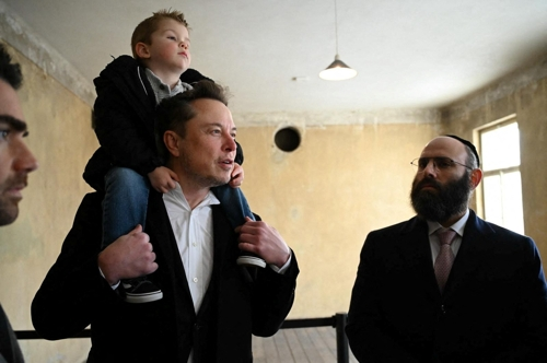일론 머스크(왼쪽) 테슬라 최고경영자가 22일 아들을 목말 태운 채 유럽 ​​유대인 협회의 랍비 메나헴 마골린 등과 함께 폴란드 아우슈비츠의 유대인 수용소를 돌아보고 있다. 로이터 연합뉴스