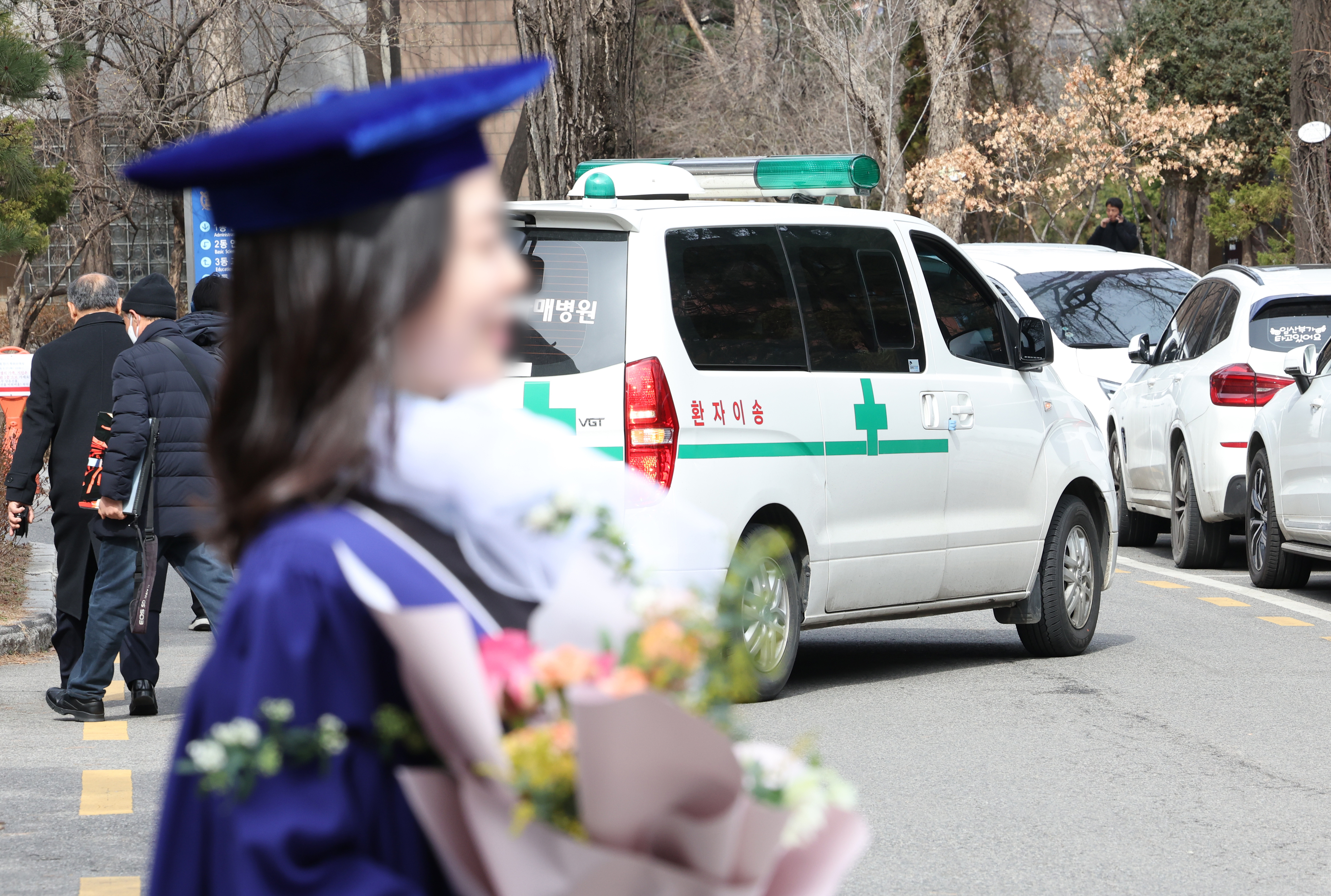 27일 오후 서울 종로구 서울대학교 의과대학에서 열린 ‘제78회 전기 서울대학교 의과대학·대학원 학위수여식’에서 기념 촬영하는 졸업생 뒤로 구급차가 지나가고 있다.  연합뉴스.