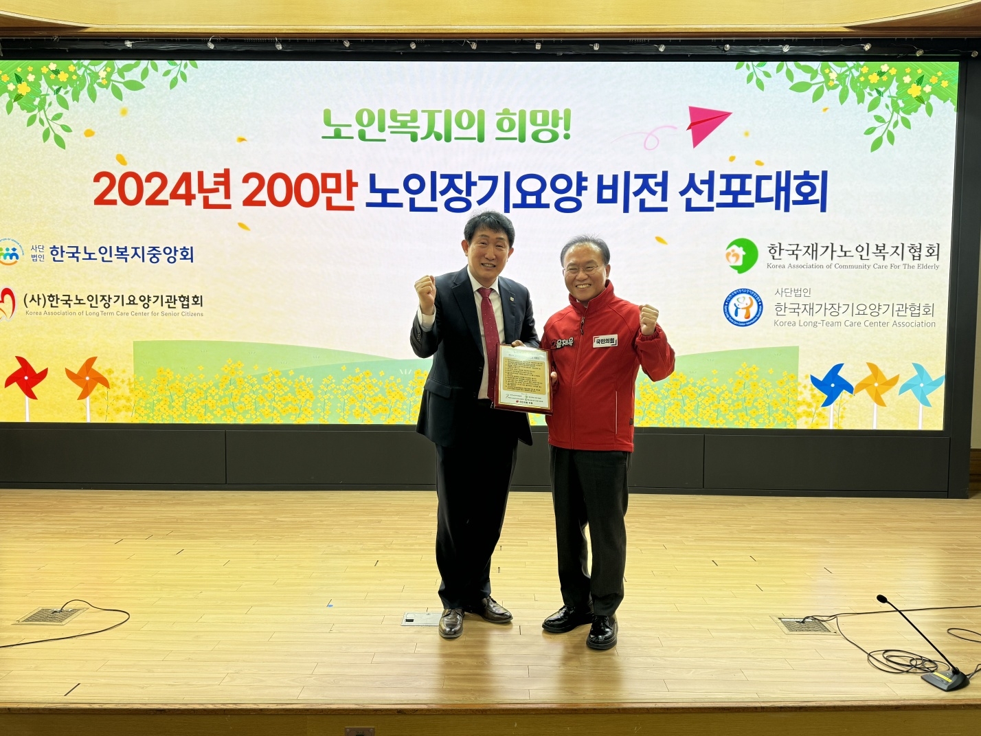 한국노인복지중앙회 권태엽(왼쪽) 회장이 19일  ‘노인복지의 희망! 200만 노인장기요양 비전 선포대회’에서 국민의힘 윤재옥 원내대표에게 12대 정책의제를 담은 명패를 전달하고 있다. 사진:한국노인복지중앙회.