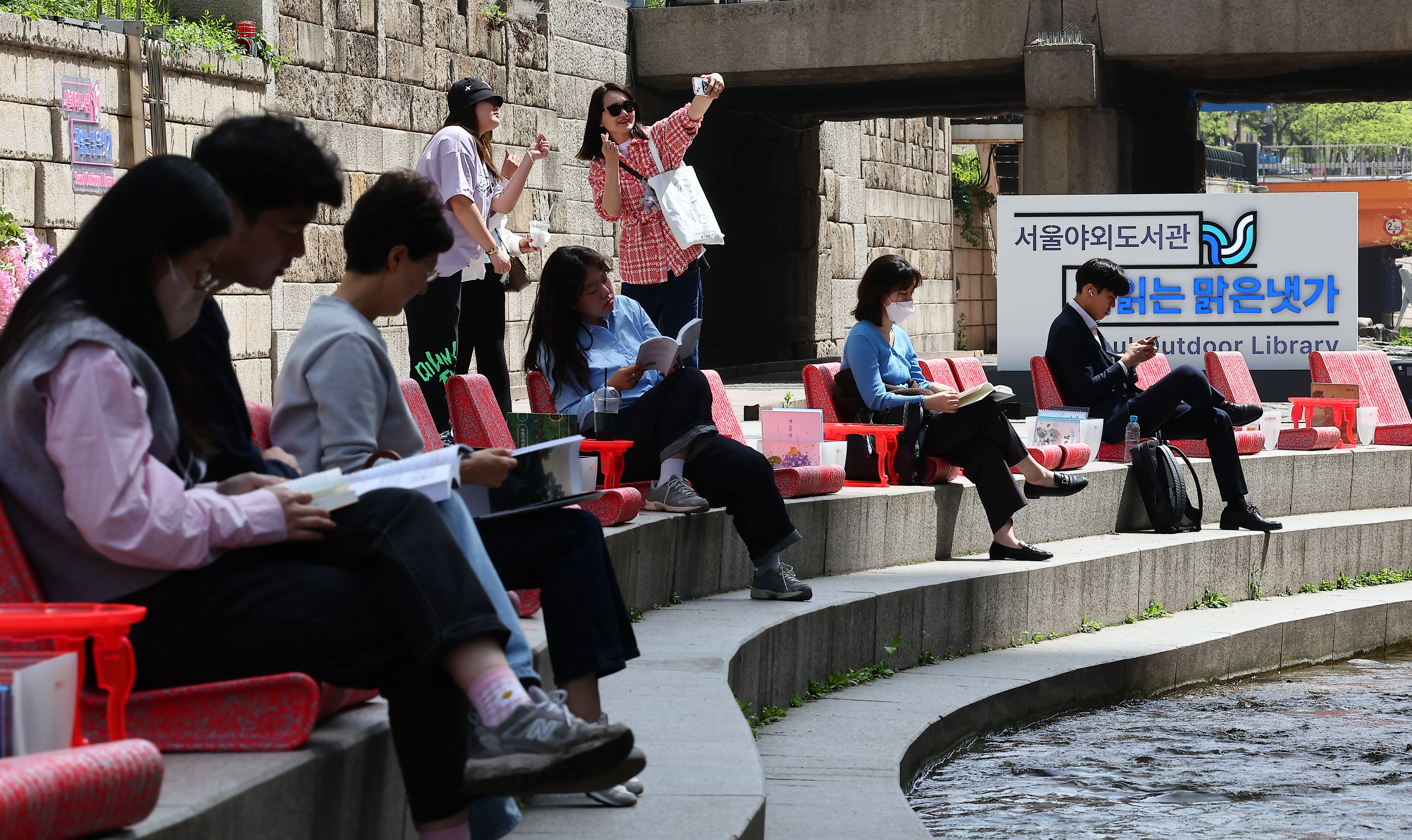 서울야외도서관 ‘청계천 책 읽는 맑은냇가’ 운영 첫 날인 지난 18일 서울 종로구 청계천에서 시민들이 독서를 즐기고 있다.   뉴시스