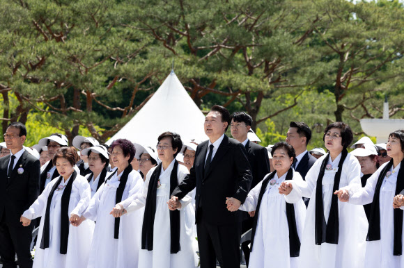 윤석열 대통령이 18일 광주시 북구 국립5·18민주묘지에서 열린 제44주년 5·18민주화운동 기념식에서 오월어머니 회원들의 손을 잡고 ‘님을 위한 행진곡’을 제창하고 있다.  2024.5.18. 대통령실 제공