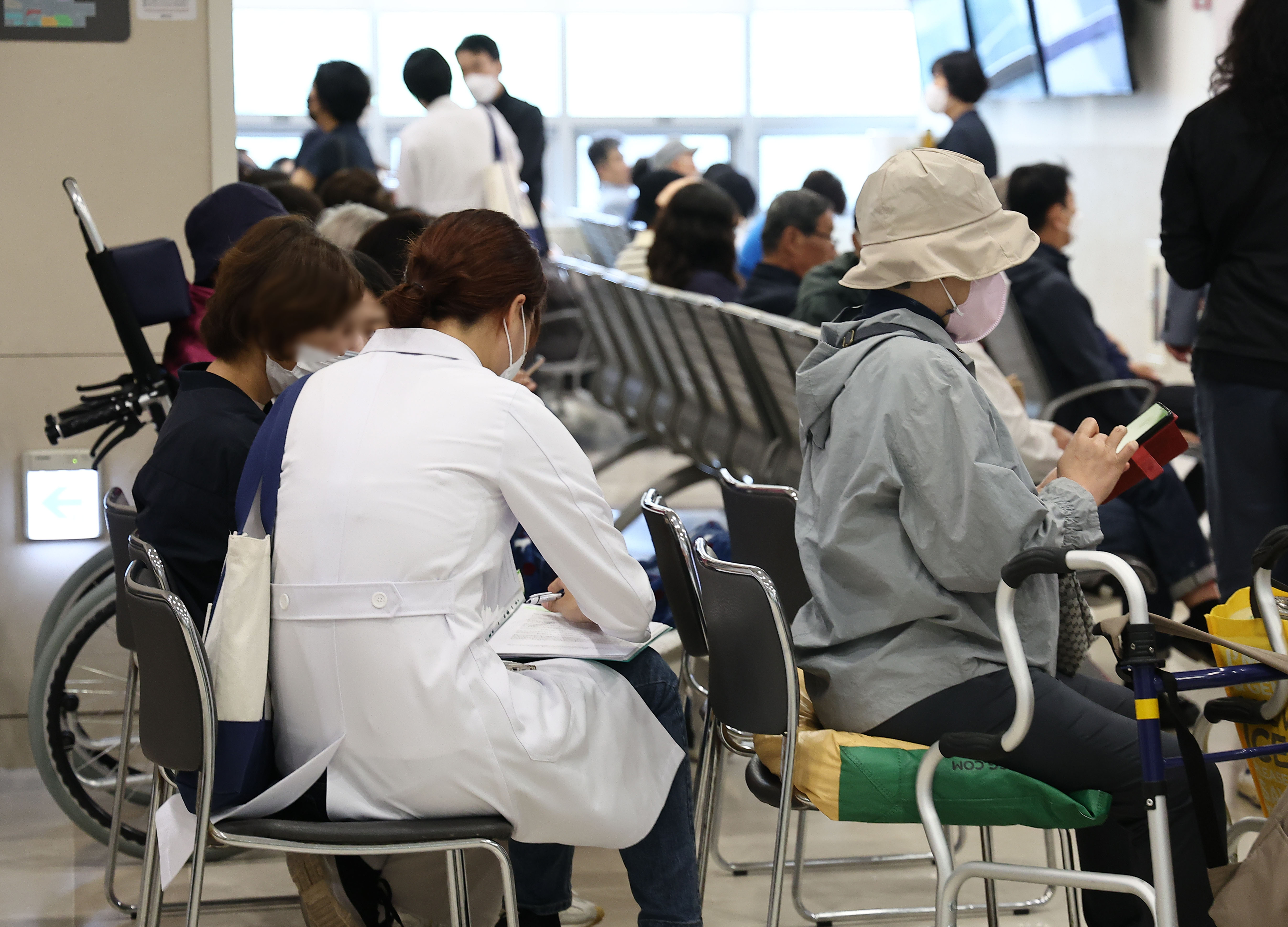 지난 22일 서울의 한 대학병원 진료실 앞에서 한 의사가 대기 중인 환자에게 다가가 진료를 보고 있다. 연합뉴스