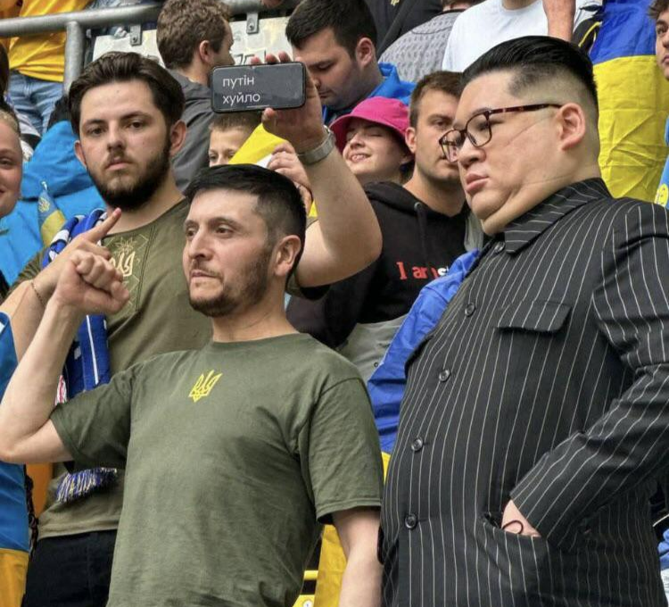 볼로디미르 젤렌스키(왼쪽) 우크라이나 대통령과 김정은 북한 국무위원장으로 변장한 관객들이 21일(현지시간) 독일 뒤셀도르프 아레나에서 열린 유로 2024 조별리그 E조 우크라이나와 슬로바키아의 경기를 함께 지켜보고 있다. 뒤의 남성이 휴대전화에 띄운 자막은 푸틴을 비하하는 뜻이다. 인스타그램 @kimjongunlookalike