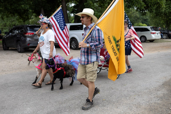 Steve Baine carries the Gadsden flag as wife Jennifer Baine leads her three year old Nigora goats Pancake and Patti at the 28th annual Pet Parade during Fourth of July Independence Day celebrations in Bandera, Texas, U.S., July 4, 2024. REUTERS 연합뉴스