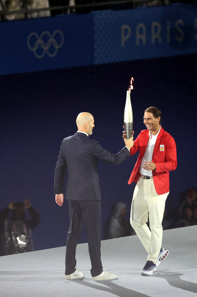 지네딘 지단이 26일(현지시간) 프랑스 파리 트로카데로광장에서 열린 2024 파리 올림픽 개회식에서 성화를 다음 주자인 라파엘 나달에게 전달하고 있다. 2024.7.27  연합뉴스