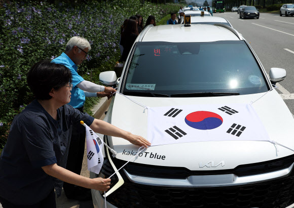 송파구청이 송파모범운전자회와 함께 13일 오전 서울 송파구 올림픽공원 인근에서 연 ‘호국영웅택시 카퍼레이드’에서 참가자들이 태극기를 택시에 부착하고 있다. 2024.8.13. 연합뉴스