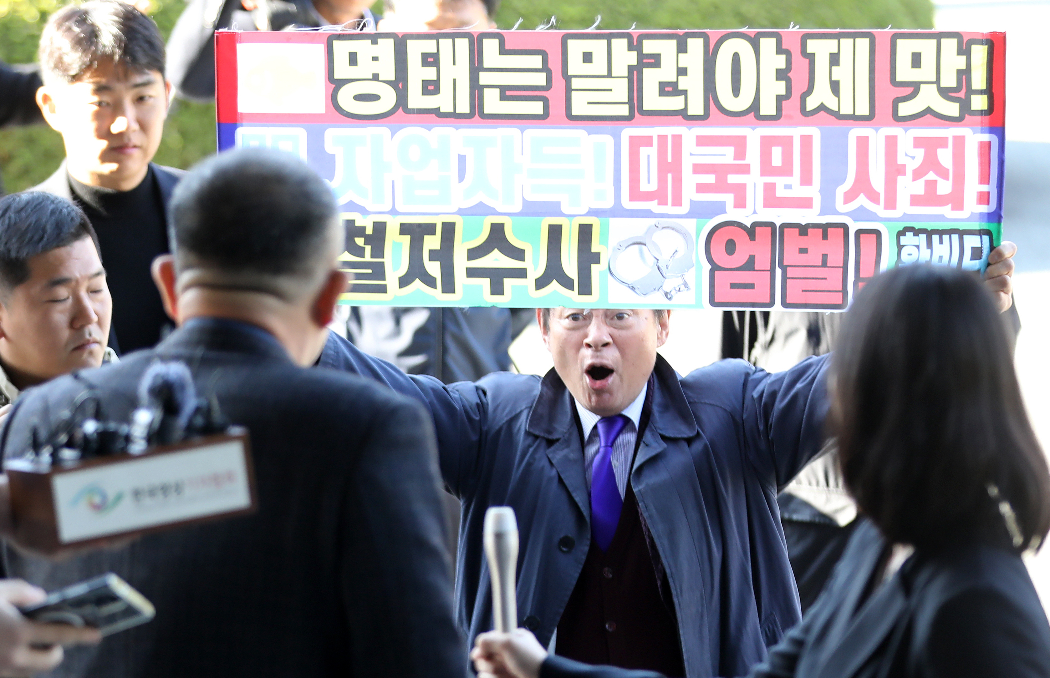 윤석열 대통령 부부 공천 개입 의혹의 핵심 인물인 명태균 씨가 9일 오전 정치자금법 위반 혐의 피의자 신분으로 검찰 조사를 받기 위해 경남 창원시 성산구 창원지방검찰청으로 출석하며 ‘명태는 말려야 제맛’ 등이 적힌 현수막을 든 한 유튜버와 실랑이를 벌이고 있다. 청사로 들어가는 명 씨 뒤에서 한 유튜버가 “어제는 꼬리내리고”라고 비난하자 명 씨는 뒤돌아서 “정신차려”라고 호통쳤다. 2024.11.9. 뉴스1