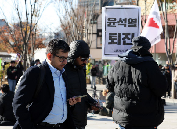 윤석열 대통령이 긴급 대국민 담화를 통해 비상계엄 해제를 선언한 4일 오전 서울 종로구 광화문광장에서 한 외국인 관광객이 계엄 반대 집회를 지나치고 있다. 2024.12.4. 연합뉴스