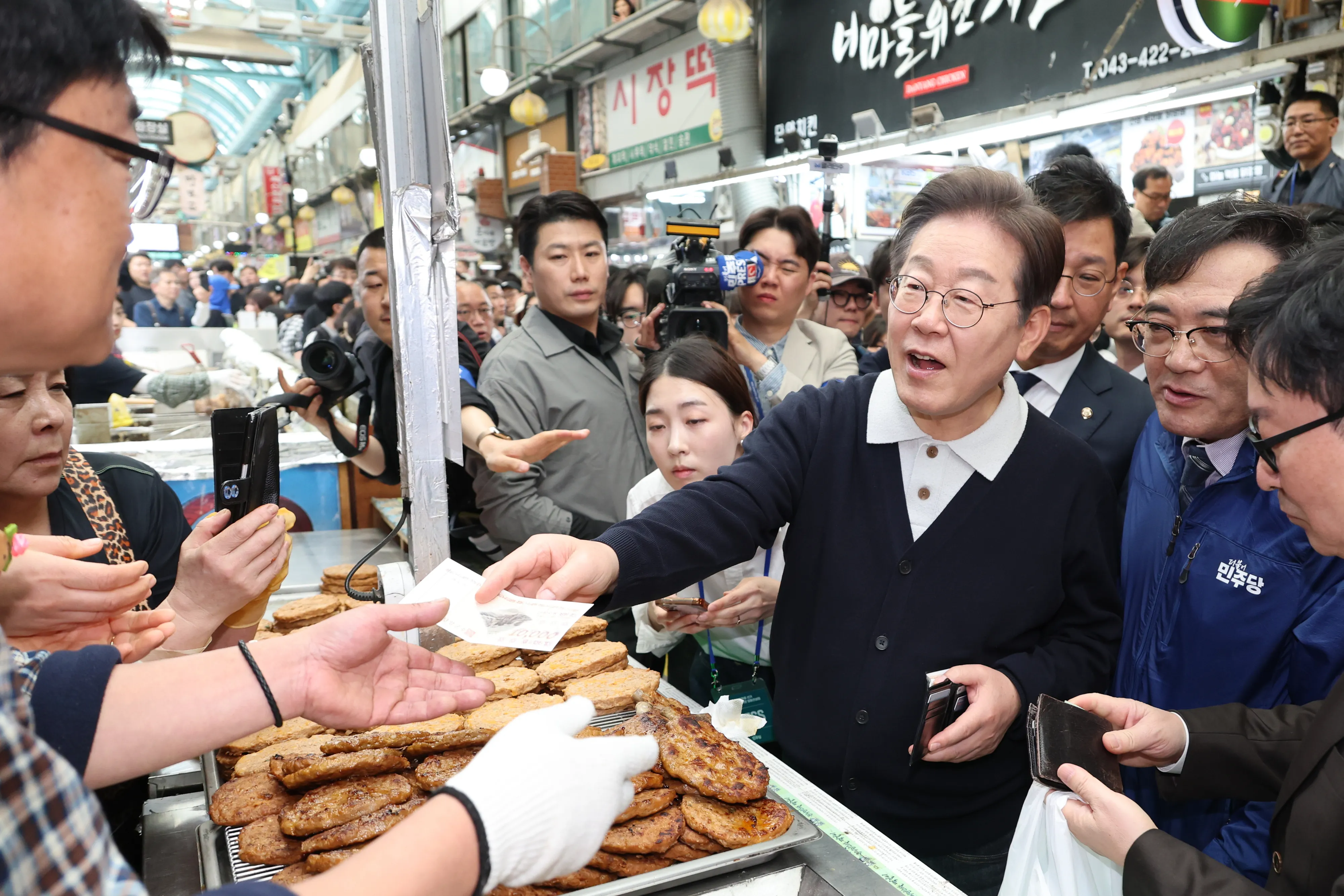 지역화폐 사용하는 이재명 후보  이재명(가운데) 더불어민주당 이재명 대선 후보가 ‘골목골목 경청 투어’ : 단양팔경 편‘에 나선 4일 충북 단양군 단양구경시장에서 떡갈비를 사 먹으면서 지역화폐를 사용하고 있다. 2025.5.4