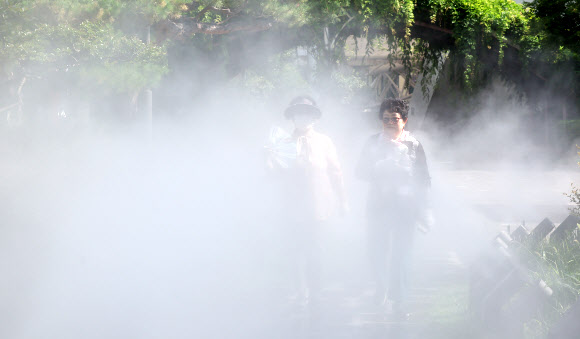 대구에 폭염경보가 발효 중인 30일 대구 중구 김광석다시그리기길 산책로에 쿨링포그(안개형 냉각수)가 가동 중인 가운데 시민들이 부채와 휴대용 선풍기를 들고 더위를 식히고 있다. 2025.6.30 연합뉴스