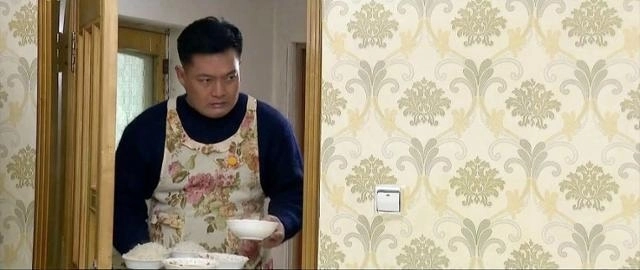 조선중앙TV 드라마 ‘백학벌의 새봄’ 속 남성이 꽃무늬 앞치마를 입고 아내와 딸에게 밥을 차려주고 있다. 조선중앙TV 캡처, 연합뉴스