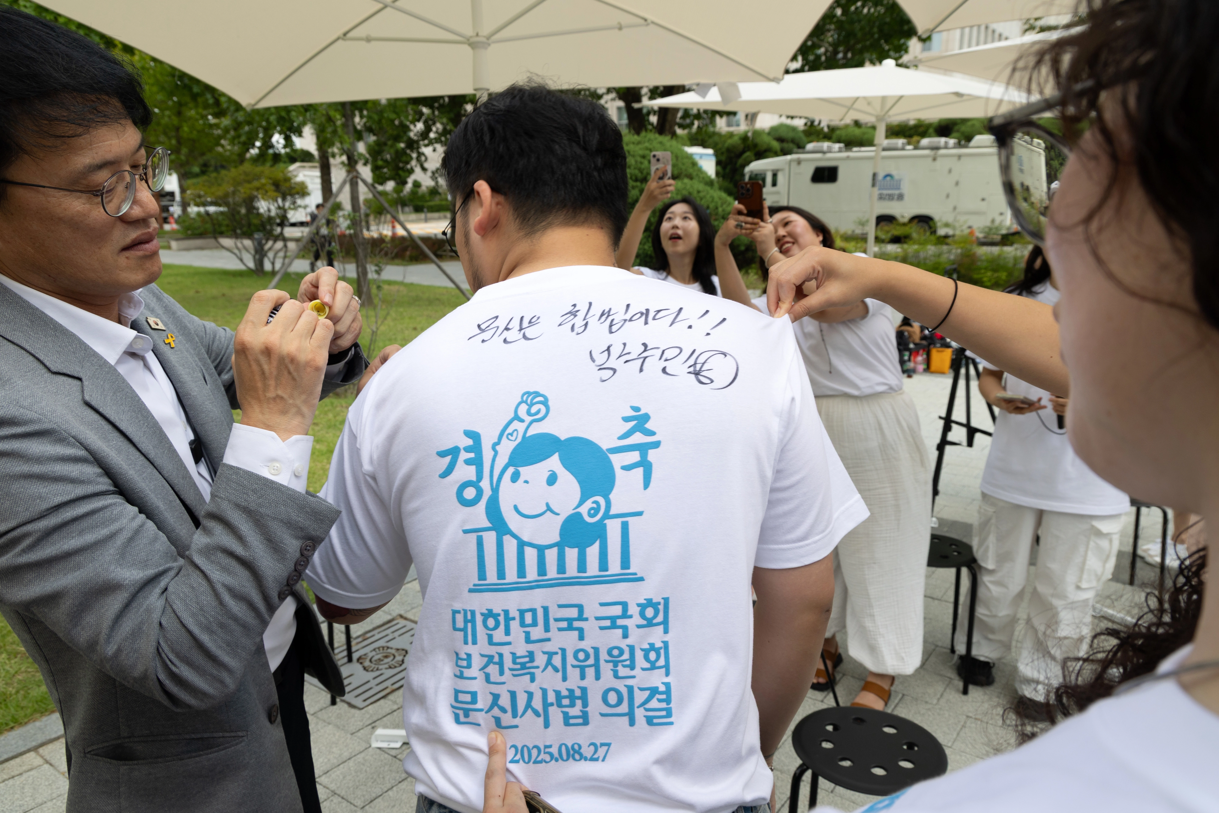 박주민 국회 보건복지위원장이 지난달 27일 국회 소통관 앞에서 열린 ‘문신사법 의결 경축’ 타투이스트들의 캐리커쳐 행사에 참석한 뒤 타투이스트의 티셔츠에 사인을 해주고 있다. 뉴스1