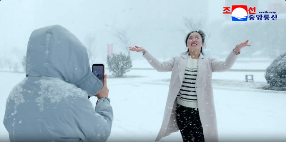 지난 4일 평양에 첫눈이 내린 가운데 한 여성이 양팔을 벌리고 포즈를 취하며 동료가 휴대전화로 촬영하고 있다. 이날 평양 지역 강설량은 평균 9cm를 기록했다고 조선중앙통신이 5일 보도했다. 2025.12.5  평양 조선중앙통신 연합뉴스