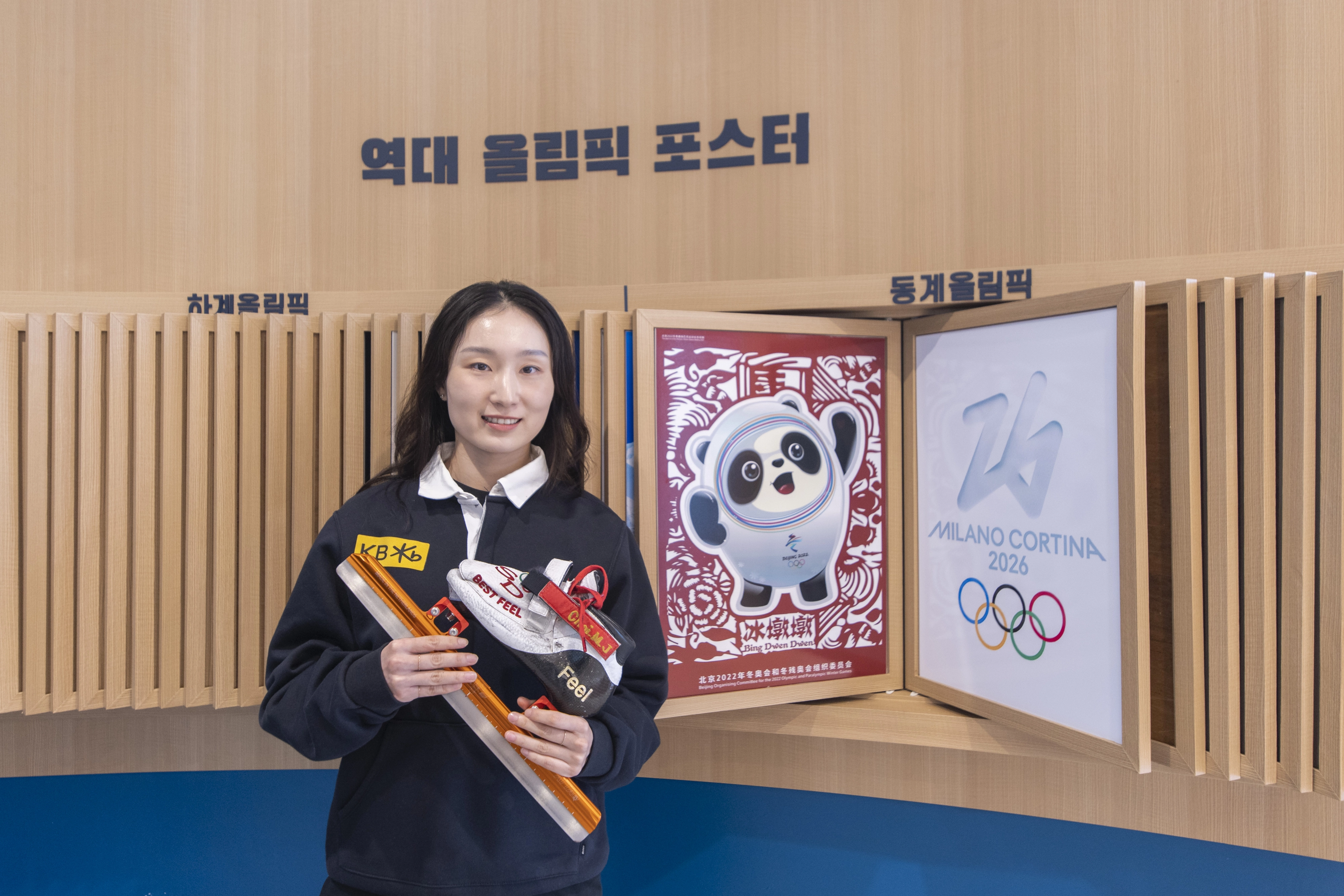 최민정이 17일 충북 진천선수촌에서 경기 때 신는 스케이트를 들고 2022 베이징 동계올림픽 포스터(왼쪽)와 밀라노·코르티나담페초 동계올림픽 포스터 옆에 서서 기념사진을 찍고 있다. 진천 류재민 기자