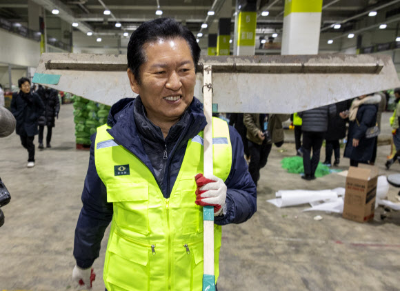 더불어민주당 정청래 대표가 7일 서울 송파구 가락동농수산물도매시장 채소2동을 찾아 경매 후 남겨진 쓰레기들을 치우기 위해 청소 도구를 어깨에 메고 이동하고 있다. 이날 민주당은 새해를 맞이해 ‘국민 곁으로! 현장 속으로!’ 현장 방문을 시작했다. 2026.1.7 연합뉴스