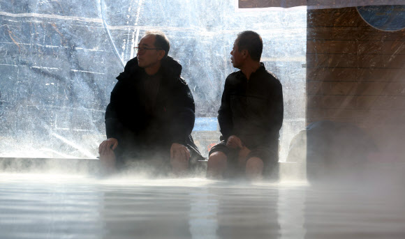 7일 낮 한파 속 충북 충주시 수안보면 온천 족욕 체험장에서 시민들이 따뜻한 온천수에 발을 담그며 한겨울 추위를 달래고 있다.  수안보 벚꽃길을 따라 조성된 이 족욕체험장에는 섭씨 47도 안팎의 온천수가 20∼40㎝ 깊이로 담겨 있다. 2026.1.7. 연합뉴스