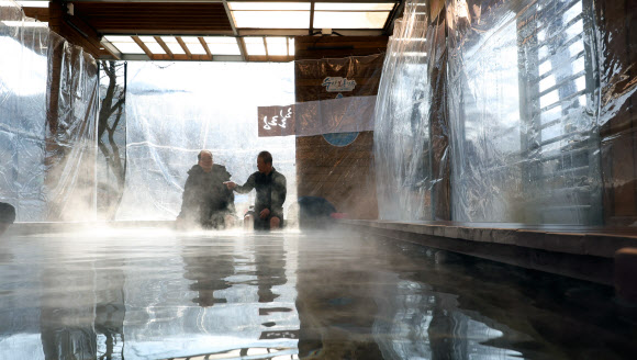 7일 낮 한파 속 충북 충주시 수안보면 온천 족욕 체험장에서 시민들이 따뜻한 온천수에 발을 담그며 한겨울 추위를 달래고 있다.  수안보 벚꽃길을 따라 조성된 이 족욕체험장에는 섭씨 47도 안팎의 온천수가 20∼40㎝ 깊이로 담겨 있다. 2026.1.7. 연합뉴스
