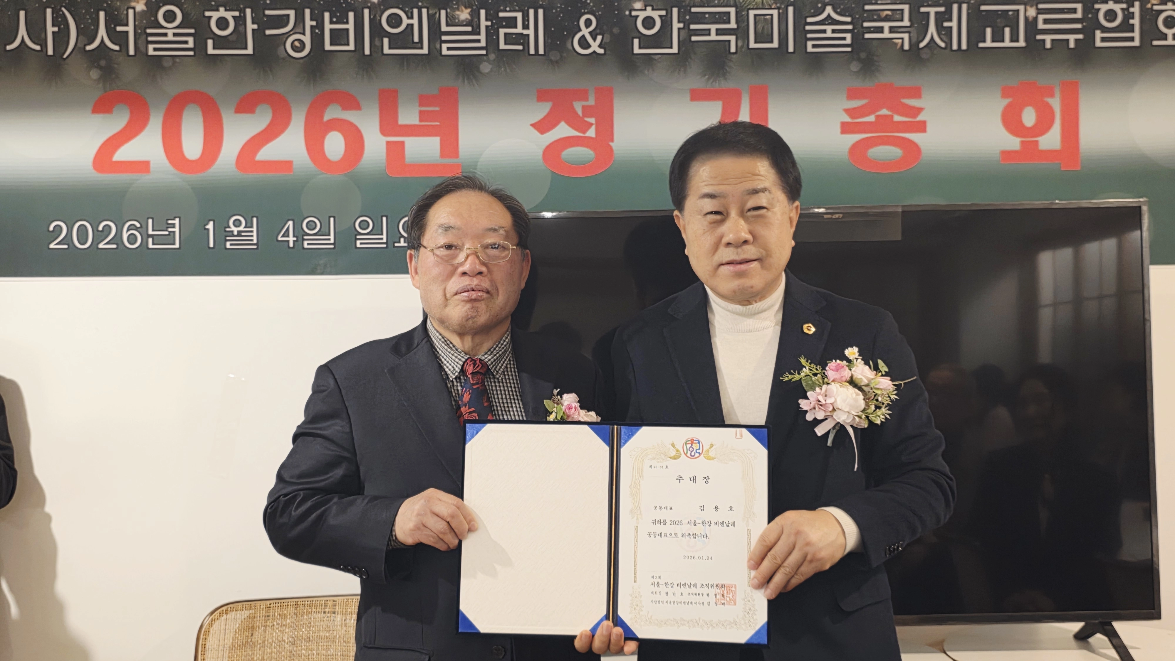 지난 1월 4일 서울 용산구 삼각지 인근 카페에서 개최된 서울한강비엔날레 ＆ 한국미술국제교류협회 2026년 정기총회에 참석한 김용호 서울시의원(오른쪽)이 공동대표 추대장을 받고 김정택 이사장과 기념촬영을 하고 있다.