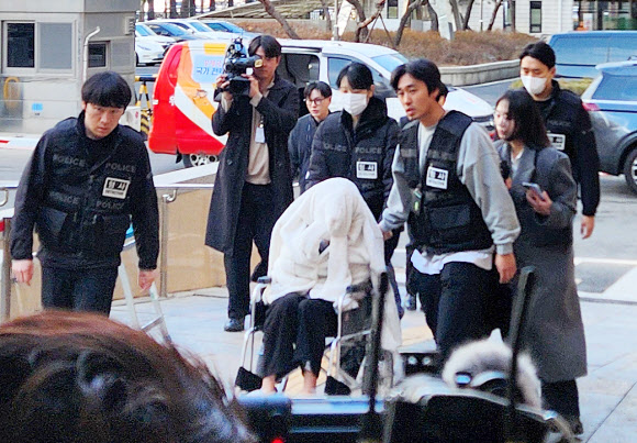 지남 25일 약에 취한 상태로 외제 SUV 차량을 몰고 반포대교를 달리다 한강 둔치로 추락한 운전자 A씨가 27일 서울 마포구 서부지방법원에서 열린 구속 전 피의자 심문(영장실질심사)에 옷으로 얼굴을 가리고 휠체어를 탄 채 출석하고 있다.  A씨는 경찰 조사에서 약물을 투약하고 운전했다며 혐의를 시인한 바 있다. 2026.2.27  연합뉴스