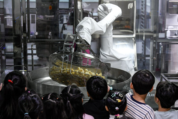 18일 경기도 수원시 대평초등학교에 설치된 거점형 학교급식 튀김 지원실에서 1학년 학생들이 튀김 조리 로봇을 살펴보고 있다. 튀김 지원실은 학생 선호도가 높은 튀김 식단을 별도 공간에서 조리한 뒤 인근 학교에 제공하기 위한 것으로 경기교육청이 전국에서 처음으로 도입한 학교급식 모델이다. 2026.3.18 [공동취재] 연합뉴스