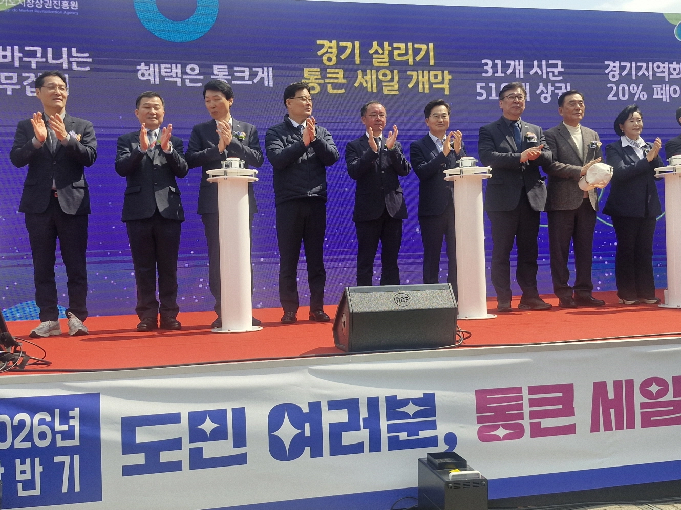 한원찬 의원이 20일 수원 남문시장에서 열린 ‘2026년 상반기 경기 살리기 통큰 세일’ 개막식에 참석해 김동연 경기도지사 등 주요 내빈들과 함께 개막을 축하하는 박수를 치고 있다.(사진=경기도의회)