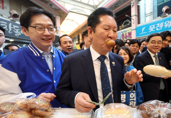 더불어민주당 정청래 대표가 23일 오후 경남 양산시 중부동 양산남부시장에서 찹쌀도넛을 먹고 있다. 왼쪽은 김경수 경남지사 후보. 2026.3.23 연합뉴스