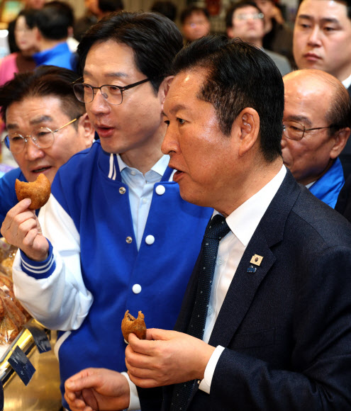더불어민주당 정청래 대표가 23일 오후 경남 양산시 중부동 양산남부시장에서 찹쌀도넛을 먹으며 상인 이야기를 경청하고 있다. 왼쪽은 김경수 경남지사 후보. 2026.3.23 연합뉴스