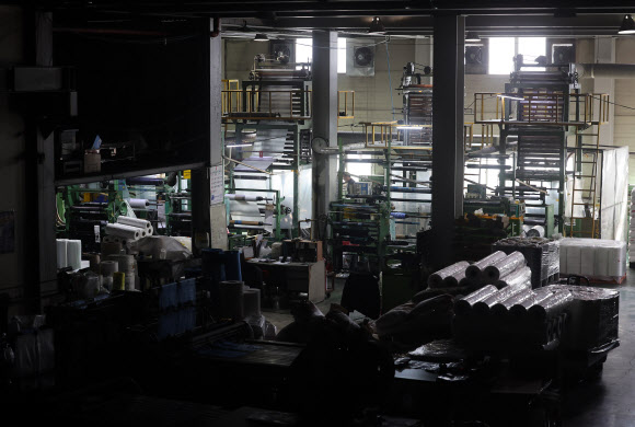 24일 중동 사태에 따른 폴리에틸렌 등 원료 수급 불안 영향으로 최근 일시적으로 인원 감축 운영에 들어간 경기 안산시의 한 비닐봉투, 종량제 봉투 제조 공장 내 가공 작업대의 불이 꺼져있다.  중동 정세 불안에 따른 나프타 도입 차질로 국내 석유화학 업체들이 감산에 나서면서 국내 플라스틱 가공업체들이 어려움에 처했다. 2026.3.24 연합뉴스