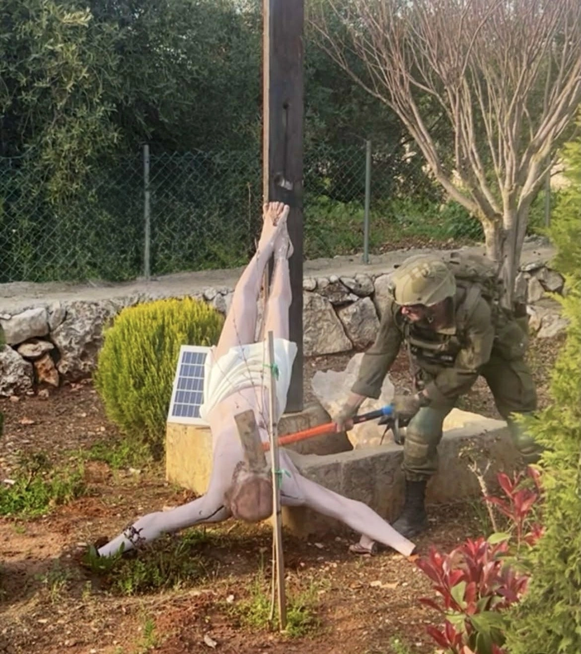 한 이스라엘 군인이 십자가에 매달려 있던 것으로 보이는 예수상의 얼굴 부분을 망치로 내리치는 사진. 2026.4.20 X 캡처